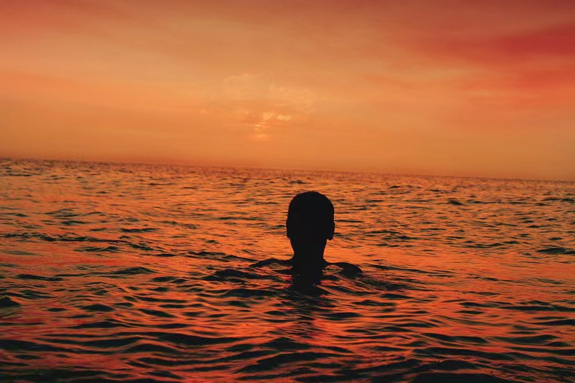 Silhouette of person in ocean during sunset.